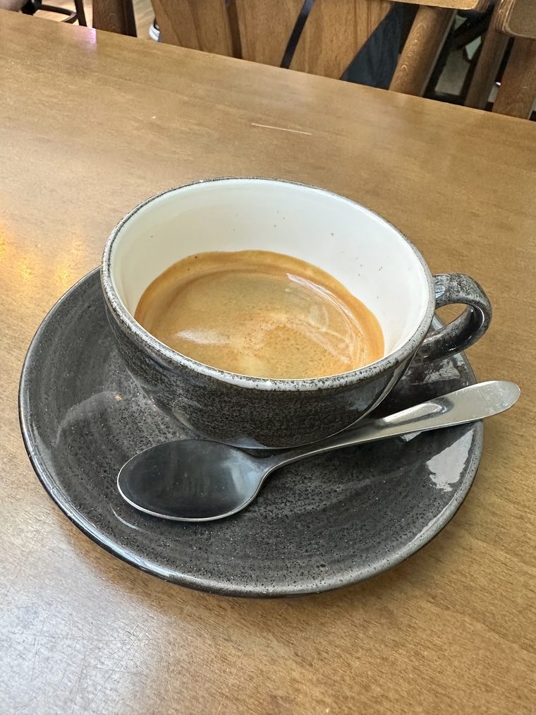 An americano in a grey cup and saucer with a spoon.
