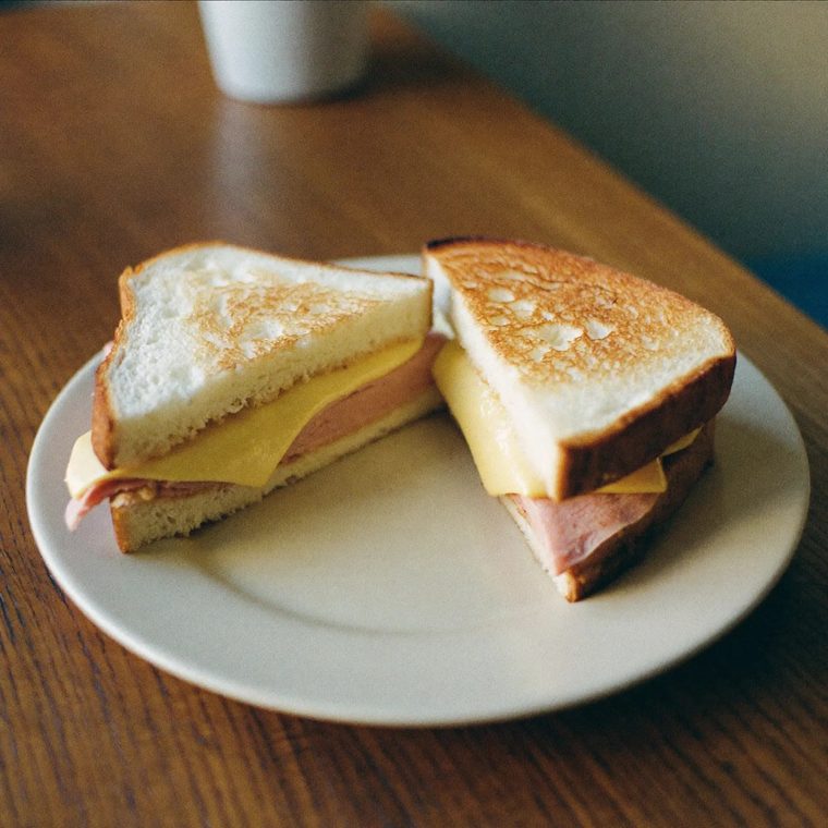 A toasted ham and cheese sandwich cut in half on a white plate.
